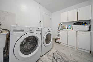 Washroom with independent washer and dryer, cabinet space, and light tile patterned flooring
