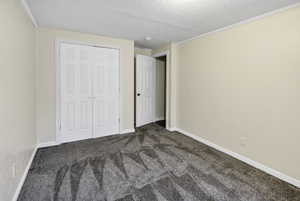 Unfurnished bedroom with dark carpet, ornamental molding, a textured ceiling, and a closet