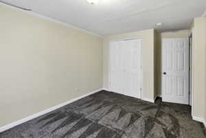 Unfurnished bedroom with dark colored carpet, crown molding, and a closet