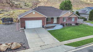 Ranch-style house featuring brick siding, an attached garage, concrete driveway, a trampoline, and a shingled roof