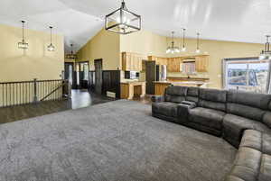 Living area featuring plenty of natural light, a chandelier, high vaulted ceiling, and dark carpet