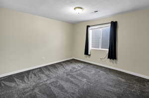 Unfurnished room featuring dark colored carpet and a textured ceiling