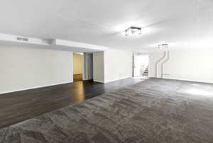Finished basement featuring stairway, dark colored carpet, dark wood-type flooring, and a textured ceiling