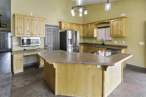 Kitchen featuring appliances with stainless steel finishes, light brown cabinets, a kitchen island, a high ceiling, and pendant lighting