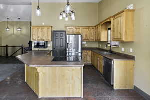 Kitchen featuring appliances with stainless steel finishes, dark countertops, a center island, light brown cabinetry, and pendant lighting