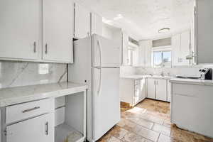 Kitchen with freestanding refrigerator, tasteful backsplash, white cabinets, light stone finish floors, and a textured ceiling