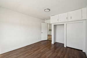 Unfurnished bedroom with a textured ceiling, dark wood-style flooring, and a closet