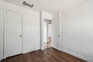 Unfurnished bedroom featuring dark wood-type flooring and baseboards
