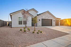 View of front of property with an attached garage, concrete driveway, stucco siding, and stone siding