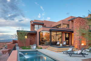 Back of property featuring a patio, an outdoor pool, a balcony, stone siding, and stucco siding