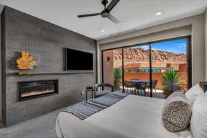 Carpeted bedroom featuring access to exterior, a glass covered fireplace, ceiling fan, and recessed lighting