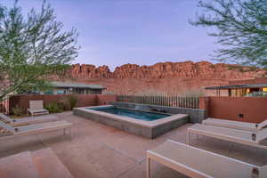 Pool at dusk with a patio area and a hot tub