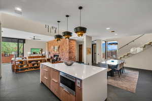 Kitchen with modern cabinets, open floor plan, a kitchen island, stainless steel microwave, and hanging light fixtures