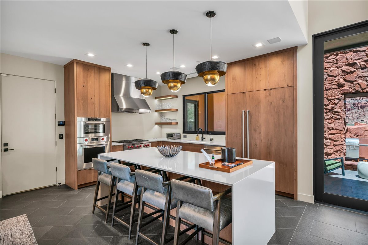 Kitchen featuring brown cabinetry, open shelves, wall chimney range hood, light countertops, and a center island