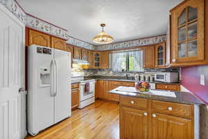 Kitchen featuring white appliances, brown cabinetry, a textured ceiling, decorative backsplash, and light wood-style floors