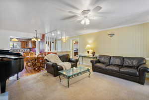 Carpeted living room featuring ornamental molding, a chandelier, and ceiling fan