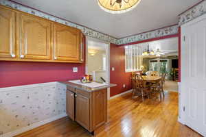 Kitchen featuring wallpapered walls, brown cabinets, light wood finished floors, a peninsula, and a textured ceiling