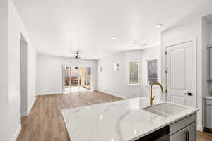 Kitchen with light wood-type flooring, an island with sink, gray cabinetry, light stone counters, and recessed lighting