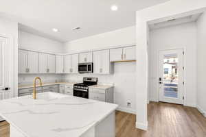 Kitchen featuring light stone counters, stainless steel appliances, light wood finished floors, an island with sink, and recessed lighting