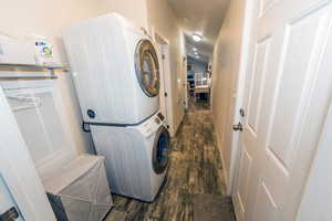 Washroom with stacked washing machine and dryer and dark wood finished floors