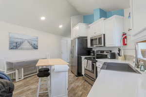 Kitchen with stainless steel appliances, white cabinetry, vaulted ceiling, a breakfast bar area, and light wood-style flooring