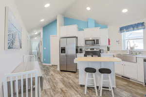 Kitchen with stainless steel appliances, lofted ceiling, a kitchen island, white cabinets, and a breakfast bar