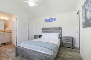 Bedroom featuring wood finished floors, lofted ceiling, connected bathroom, and a ceiling fan