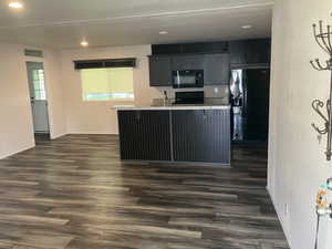 Kitchen with black appliances, dark wood finished floors, a kitchen breakfast bar, a kitchen island with sink, and recessed lighting