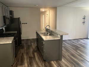 Kitchen featuring range with gas cooktop, a kitchen island with sink, gray cabinetry, and light countertops