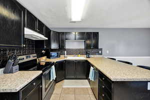 Kitchen with appliances with stainless steel finishes, dark cabinets, and light tile patterned floors