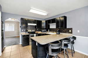 Kitchen with decorative backsplash, dark cabinets, stainless steel appliances, light countertops, and a peninsula