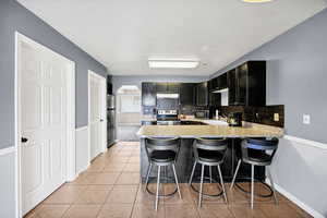 Kitchen with light countertops, light tile patterned floors, a peninsula, tasteful backsplash, and appliances with stainless steel finishes