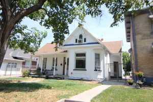 View of front of house with a gate, covered porch, brick siding, roof with shingles, and a chimney