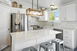 Kitchen featuring appliances with stainless steel finishes, decorative light fixtures, a kitchen bar, and white cabinets