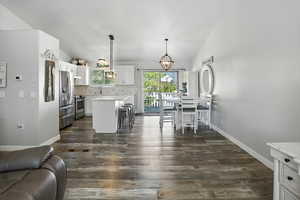 Kitchen with white cabinets, vaulted ceiling, stainless steel appliances, decorative backsplash, and decorative light fixtures