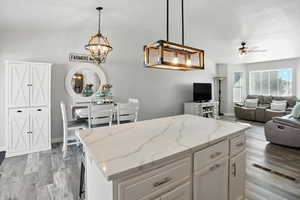 Kitchen with light stone countertops, a kitchen island, open floor plan, light wood finished floors, and white cabinetry