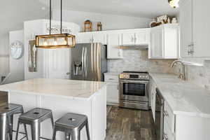 Kitchen featuring decorative backsplash, appliances with stainless steel finishes, a breakfast bar, a center island, and lofted ceiling