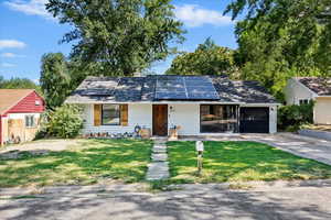 Ranch-style home with driveway, roof mounted solar panels, a front lawn, and a garage