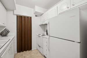 Kitchen featuring white appliances, under cabinet range hood, white cabinetry, and light countertops