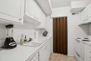 Kitchen with white electric range oven, white cabinetry, light countertops, and under cabinet range hood