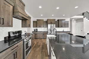 Kitchen with stainless steel appliances, ventilation hood, recessed lighting, decorative backsplash, and dark stone counters