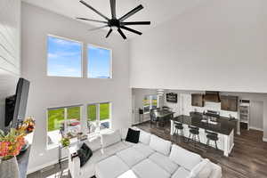 Living room with a towering ceiling, a ceiling fan, and dark wood finished floors