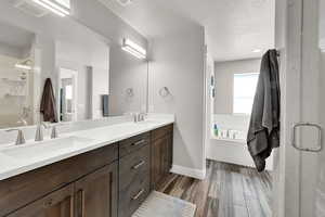 Bathroom with a garden tub, double vanity, a shower stall, wood finished floors, and a textured ceiling