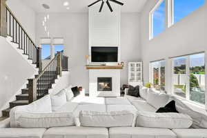 Living room with a towering ceiling, stairs, ceiling fan, and a fireplace