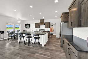 Kitchen featuring dark countertops, backsplash, recessed lighting, a center island with sink, and premium range hood
