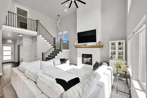 Living area with a high ceiling, a ceiling fan, a fireplace, wood finished floors, and stairway