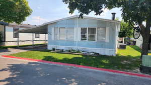 Manufactured / mobile home featuring an attached carport, a front lawn, and concrete driveway