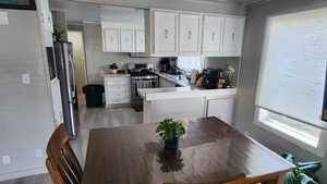 Kitchen featuring stainless steel appliances, a peninsula, white cabinets, light countertops, and light wood finished floors