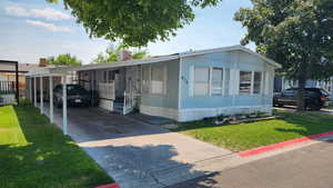 Manufactured / mobile home with a carport, concrete driveway, and a front lawn