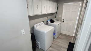 Laundry area featuring independent washer and dryer, cabinet space, and light wood-style flooring
